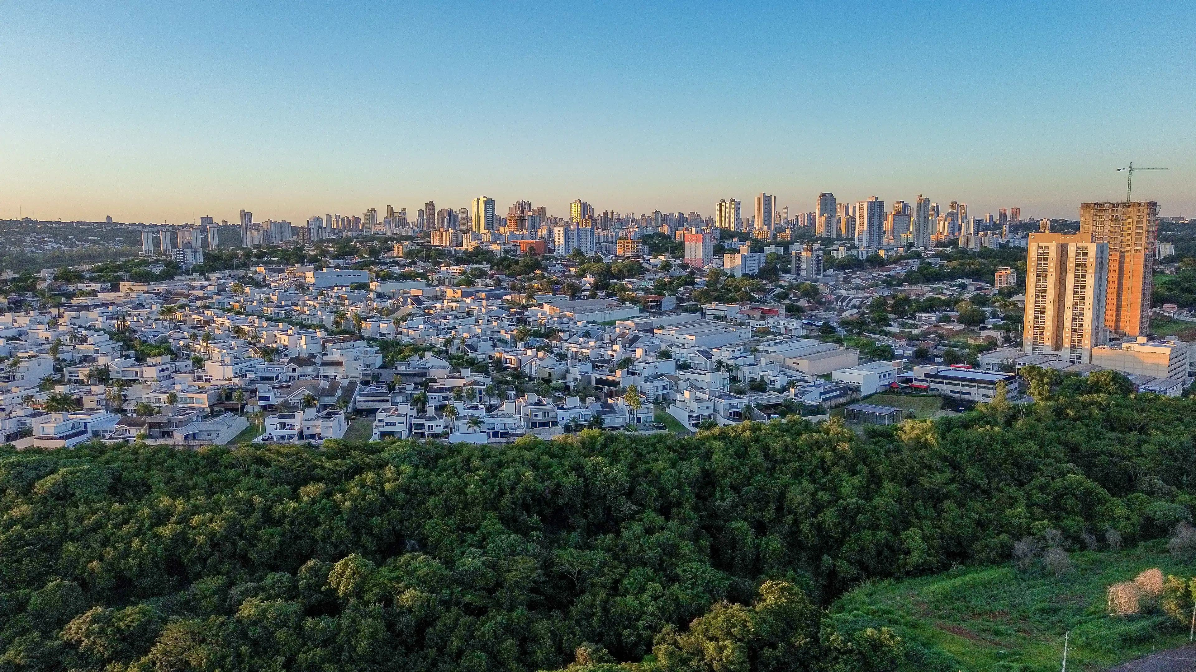 Vista aérea de um lago cercado de árvores em um parque urbano ao entardecer.